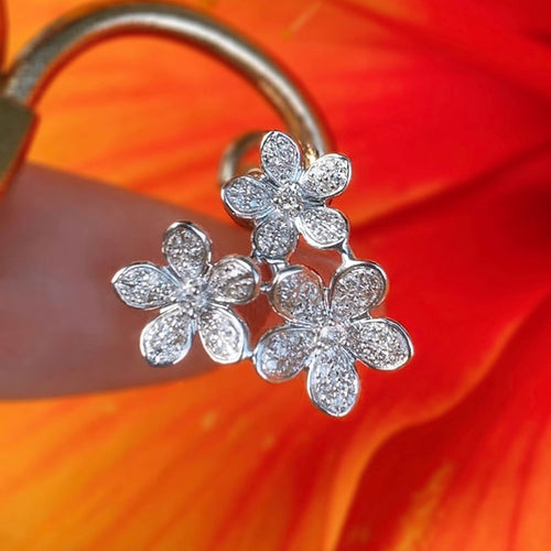 Close-up of silver triple flower pavé earring on finger with orange bloom