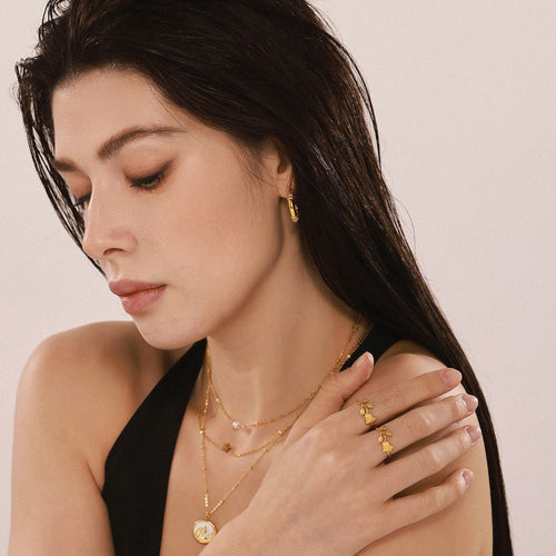 Model wears dual gold rosebud open rings with layered necklaces