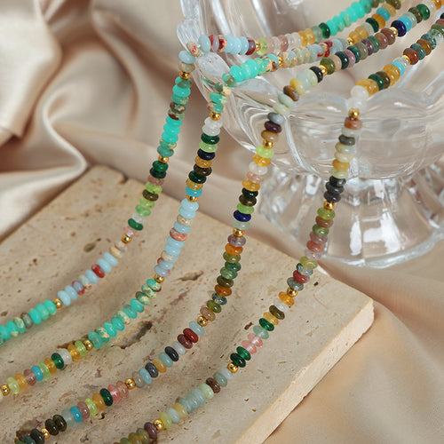Several multicolor disc stone bead necklaces draped on stone and glass