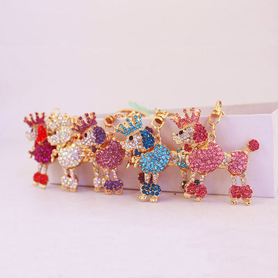 Five crowned poodle accessories in white, purple, blue, pink, and red tones stand beside a white block.