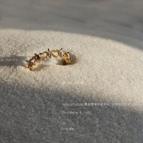 Close-up gold heart-link open ring with clear stones in sun