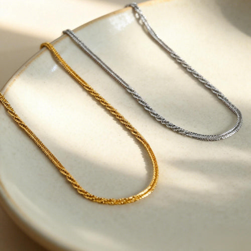 Gold and steel twisted sparkle necklaces resting on a cream ceramic plate
