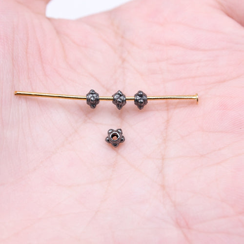 Close-up of tiny flower spacer beads showing tiny dark flower forms with central threading holes