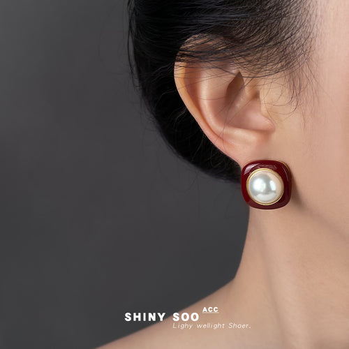 Pair of red square pearl studs on cream surface