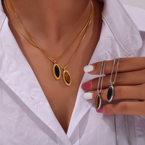Model wearing layered gold oval stone pendants holding steel oval necklaces
