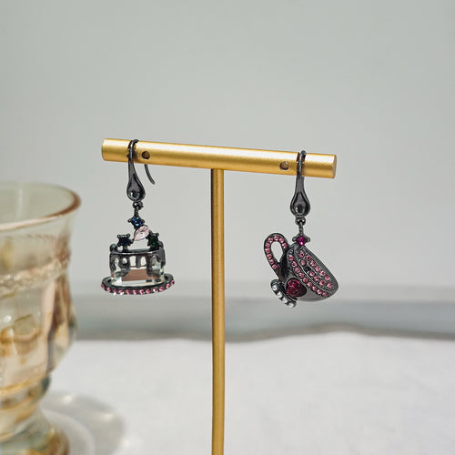 Gunmetal teacup cake earrings hanging on gold T-bar stand