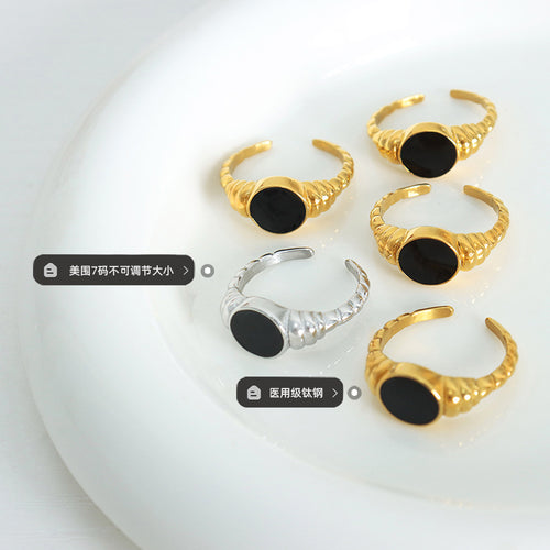 Gold and steel open rings with black ovals on white dish with labels