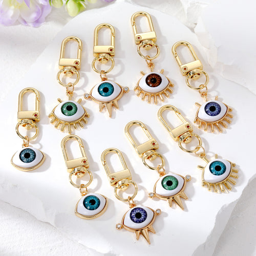 Assorted gold evil eye keychains spike lash and framed styles on white stone