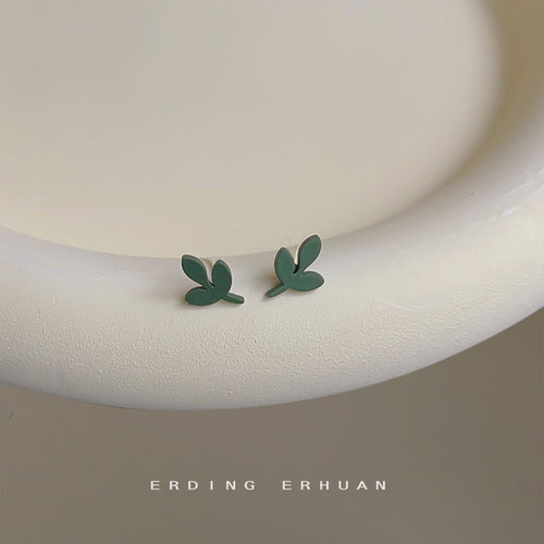 Matte green mini leaf studs on white ceramic ring surface