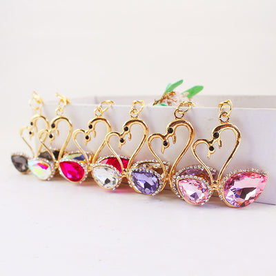 Six gold-tone double-swan pieces are lined up with black, iridescent, magenta, clear, purple, and pink wing stones.