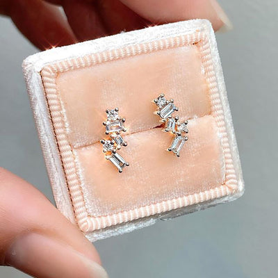 Silver geometric baguette studs in a peach velvet ring box held by fingers
