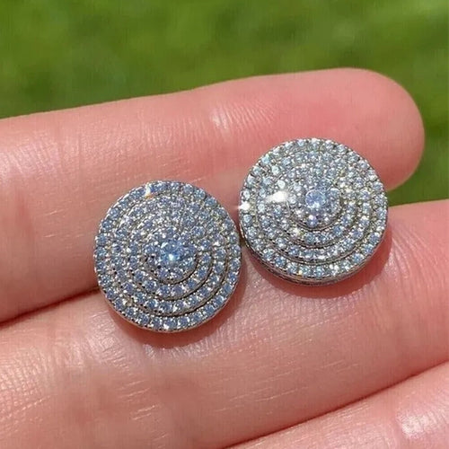 Round pave disc studs held on fingertips against green outdoor backdrop