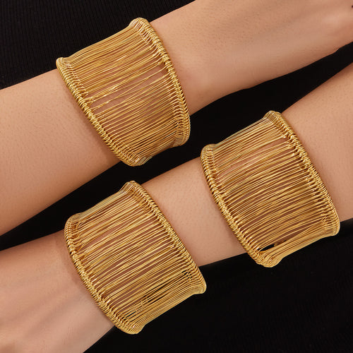 Three gold wire cuff bangles stacked on arms against black