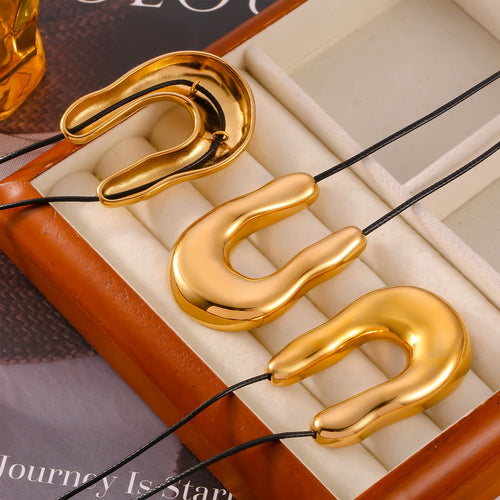 Three gold U pendants with black cords in jewelry tray