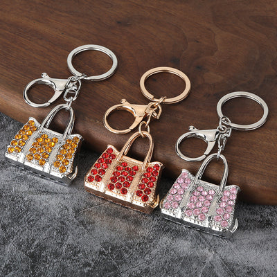Three handbag-shaped keychains with orange, red, and light pink rhinestones on a dark wood surface.