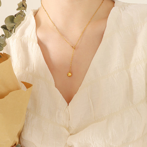 Model in white blouse wearing gold Y lariat paperclip necklace with ball drop