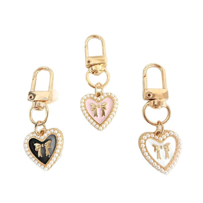 Three heart pendant keychains in black, pink and white with gold bows and pearl borders