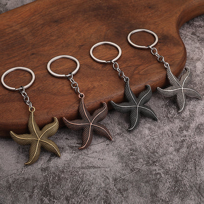 Four starfish keychains in bronze, copper, dark gray, and silver finishes displayed together.