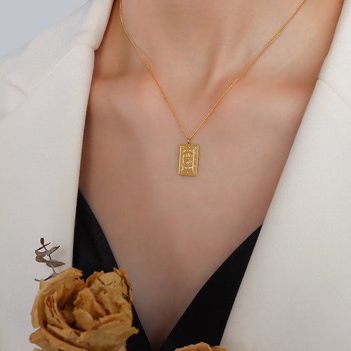 Gold sunburst rectangular pendant necklace worn with white blazer