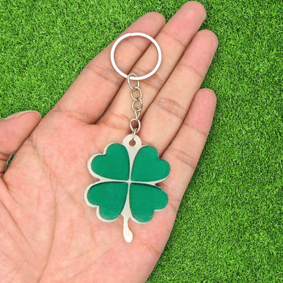 Green acrylic four leaf clover keychain held in palm on grass background