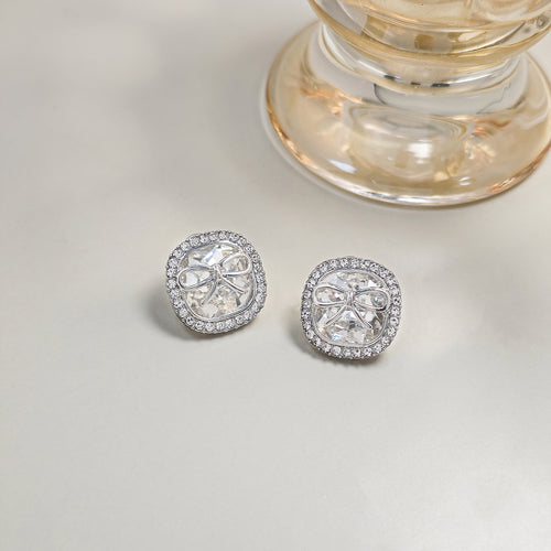 Silver square crystal bow studs on pale surface with glass base