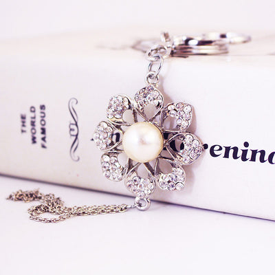 Close-up of the stone-covered flower and pearl-like center bead beside a loose chain tassel.