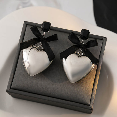 Silver heart black bow drop earrings standing on gray jewelry box