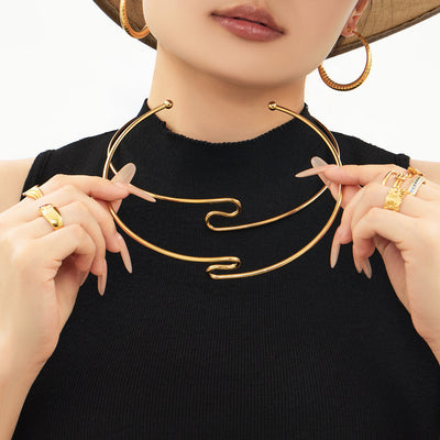 Model holding two gold S-shape open chokers at the neck