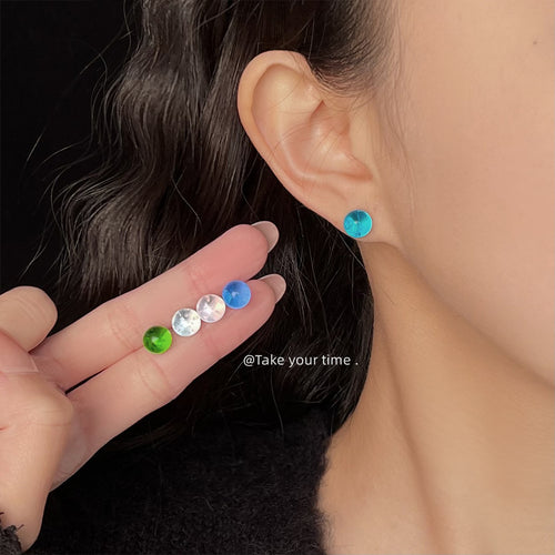 Light blue glass ball stud worn on ear with other colors in hand