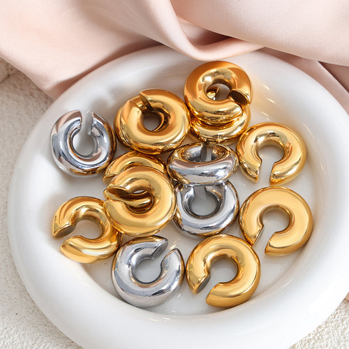 Gold and steel C-shape ear cuffs stacked in a white ceramic dish