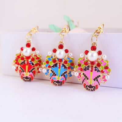 Three gold-tone opera face charms in red, blue, and pink displayed side by side.