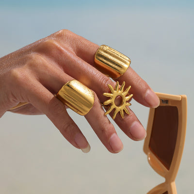 Hand wearing gold wave ridged rings and sun ring by the beach
