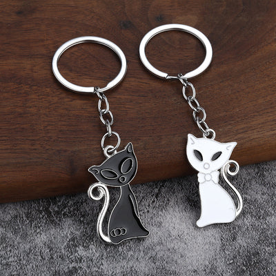 Black and white curled-tail cat keychains displayed together on wood and gray fabric.