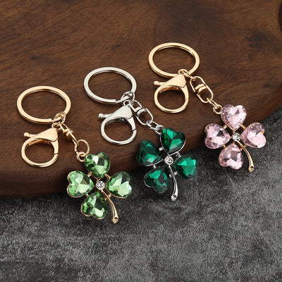 Three clover keychains with light green, dark green, and pink faceted heart-shaped leaves on a wood surface.