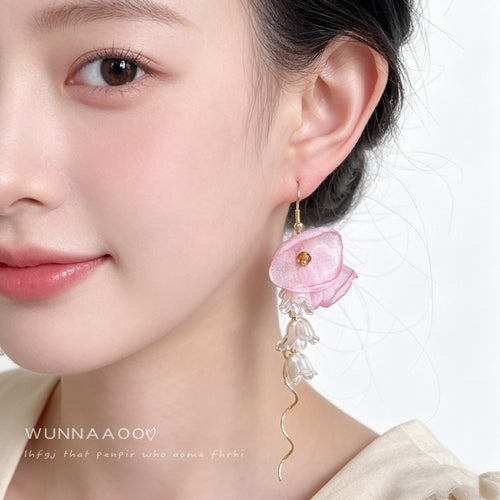 Gold-tone pink-flower white-blossom long-wire hooks shown worn on an ear.