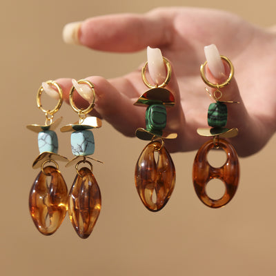 Hand holding two gold pairs of amber resin dangle earrings with blue and green stone beads