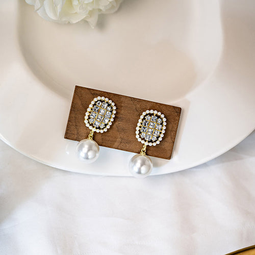 Gold oval crystal pave pearl drop studs on wood block on white plate