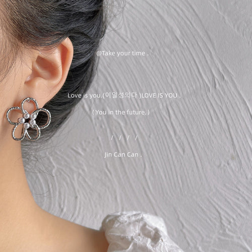Silver-tone open-five-petal pearl-center studs shown worn on an ear.