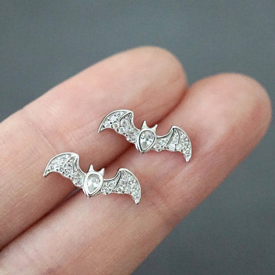Silver pave bat stud earrings pair on fingertips against gray