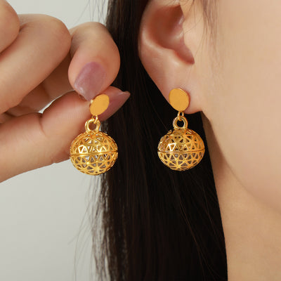 Gold filigree hollow sphere dangle earrings held near model ear