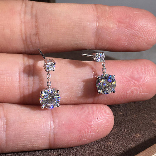 Pair of silver clear drop earrings resting on fingers
