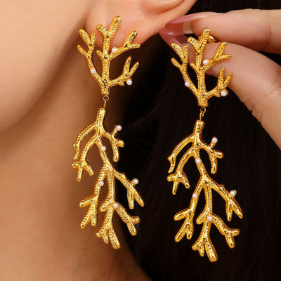 Model holding gold coral branch pearl drop earrings near ear