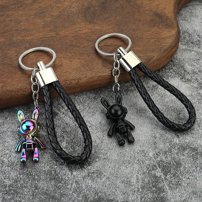 Two rabbit astronaut keychains in rainbow and black finishes on a gray surface.