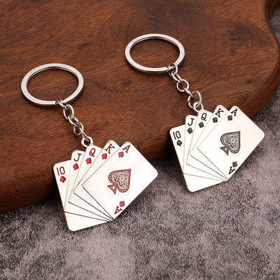 Two metal playing card keychains with red heart and black spade royal flush designs on a wooden surface.