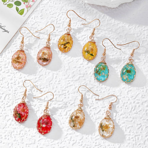 Five pairs of wire-wrapped teardrop dried flower resin earrings on white surface