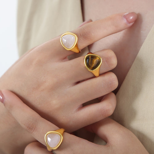 Hands wearing gold triangle pink crystal and tiger eye signet rings
