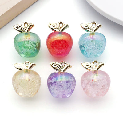Iridescent apple charms arranged on a light background