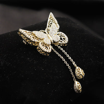 Front view of gold filigree butterfly brooch with twin teardrop chain drops against a white background.