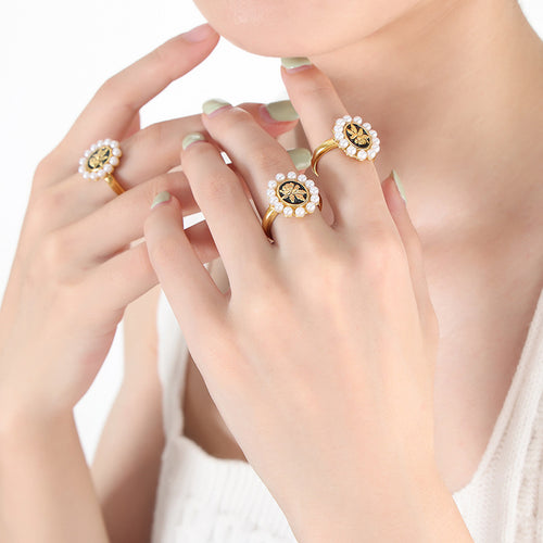 Hands wearing three gold pearl halo black enamel flower rings