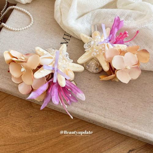 Two starfish shell flower duckbill clips on canvas book near pearls